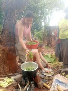 American tourists preparing traditional green vegetable local dishes with a Ugandan community during a cultural safari experience.